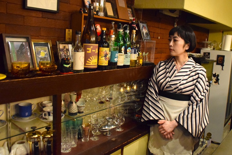 Utsugi habla sobre sus sentimientos hacia sus clientes frente a un estante que muestra su vajilla y accesorios favoritos.