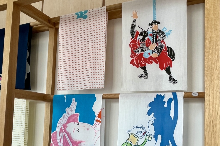 Un tenugui (toalla de mano japonesa) con un dibujo en clave. En la esquina superior derecha se ve una hormiga sosteniendo una espada, que significa "gracias".